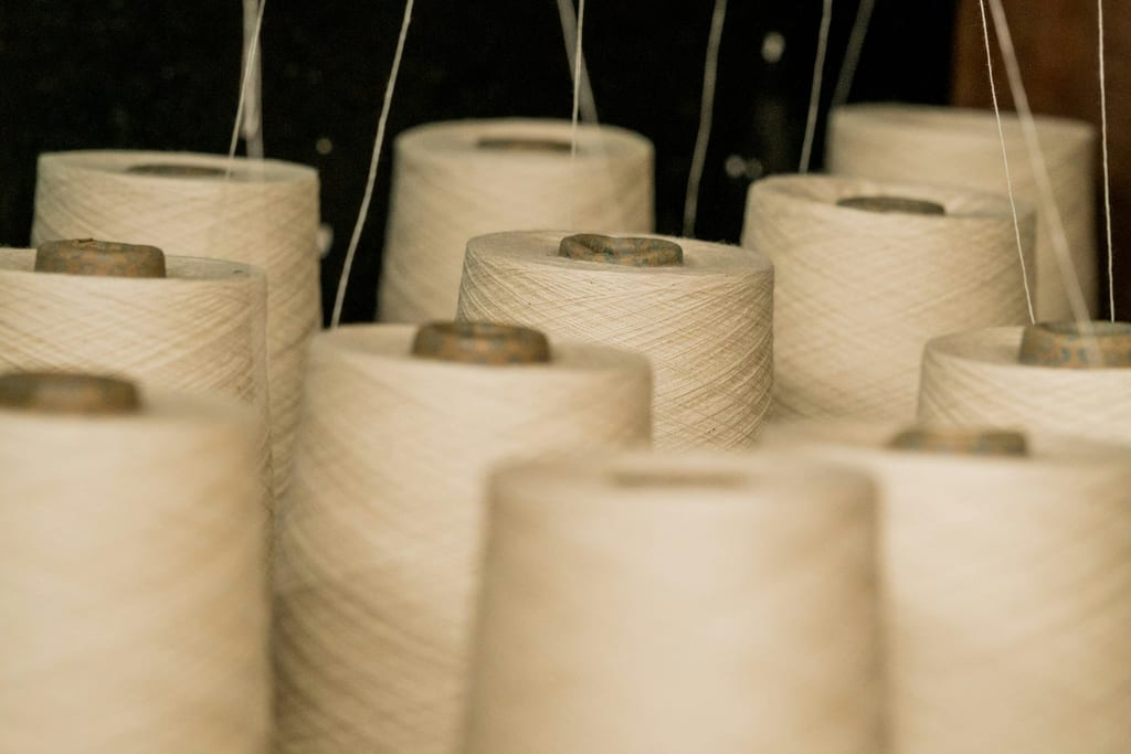 Cream-toned industrial yarn cones under soft light (representative)